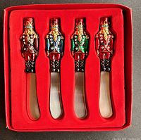 Four nutcracker-themed canape spreaders neatly arranged in gift box with red interior lining showing colorful handles and steel blades