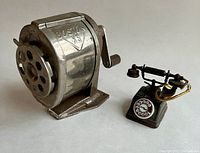 Photo showing both the Boston VS manual pencil sharpener and miniature telephone pencil sharpener side by side on a white surface.