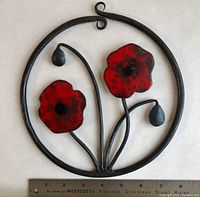 Close-up of the vintage wrought-iron circular wall hanging with red enamel poppy flowers and buds, showing approximate size with ruler