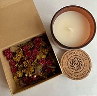 Photo of the brown glass candle jar with white wax inside, cork lid beside it, and an open cardboard box filled with mixed colored potpourri