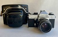 Front view of Praktica LLC 35mm camera with Pentacon electric 50mm f/1.8 lens attached and black vintage case beside it.
