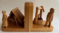 Pair of hand-carved wooden bookends with elderly rural couple figurines and traditional oven and well structures, side view showing detailed carving.