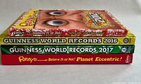 Side view showing stack of four hardcover books, including Ripley's Believe It or Not! special edition 2012, Guinness World Records 2016 and 2017, and Ripley's Planet Eccentric.