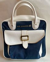Front view of the vintage Air Canada flight bag showing navy blue body with white trim, front flap pocket with buckle, and Air Canada logo in gold.