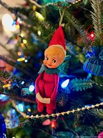 Elf tree ornament hanging on Christmas tree among lights and decorations.