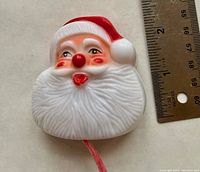 Vintage plastic Santa Claus brooch next to ruler to show size, about 2.5 x 2.25 inches.