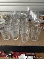 Full view of short clear glass tumblers with thick bases arranged in rows on a cardboard surface, totaling 20 pieces.