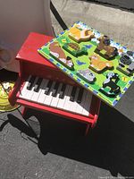 Photo showing red toy piano with white and black keys and wooden animal puzzle on top of it featuring colorful animal pieces.