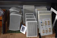 Overview of 10 white Sonance ceiling mount speakers and 2 Sonance exterior mount speakers with their corresponding grills and two Elan control panels with binding posts.