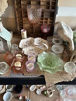Overview of Depression glass storage bowl with lid, large pink and red goblets, porcelain appetizer plates, various crystal tea light candle holders and small glass items on table.