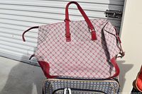 Photo of beige and red patterned fabric handbag with red leather trim and handles against a metal backdrop.