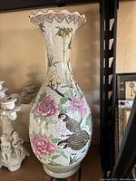 Full front view of tall porcelain vase showing bird and peony floral artwork with scalloped top edge.