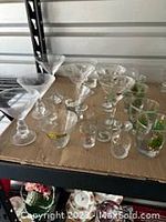 Wide view of assorted large martini glasses, shot glasses, and holiday-themed glasses arranged on cardboard.