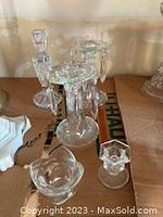 Seven clear crystal candle stick holders and decorative pieces placed on cardboard, varying sizes, some with multiple holders and different designs.