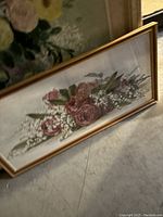 Horizontal framed floral painting with pink and white flowers leaning on floor.