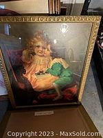 Vintage framed print showing a young girl with blonde hair in pink dress holding a cherub wearing green outfit resting on her lap.