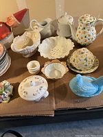 Wide angle showing multiple porcelain, pottery and glassware serving pieces including tea pot, butter dish, pitchers, and blue hen covered dish