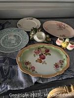 Photo showing a variety of vintage ceramic plates with floral designs placed on a dark patterned fabric.