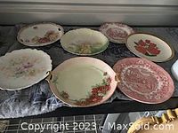 View of seven vintage decorative plates arranged on a cloth surface, showing colors and sizes.