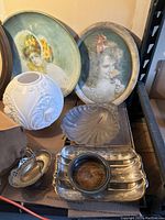 Image showing vintage decorative trays, including two painted oval trays with portraits, silver plated items such as a rectangular tray, wine coaster, shell dish, and lidded basket bowl, along with a pewter tray.