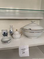 Photo showing five pieces of white china serveware including a soup tureen with lid and ladle, sugar bowl with lid, small vase with blue floral design, and two small decorative bowls.