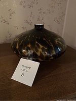 Side-angle photo showing the broad, rounded shape of the vase and its unique black and amber mottled pattern.