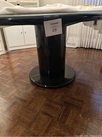 Close-up of cylindrical pedestal base and underside of tabletop showing glossy black finish.