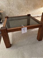 Square oak wood frame end table with smoked glass top, photographed from a low side angle showing thickness of legs and wood grain.