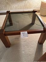 Square oak framed end table with smoked glass top shown from two angles on carpet.