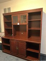 Front view of the large wooden office cabinet showing multiple open shelves, two small glass doors with brass handles, and a lower cabinet with double wooden doors.