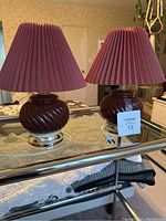 Front view of the two small table lamps with pleated burgundy shades sitting on a glass table.