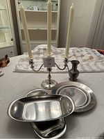 Photo showing silver plated three-arm candelabra, small pewter vase, two round stainless steel dishes, and two oval divided stainless steel dishes on a table.