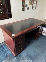 Wooden office desk viewed from left side showing leather inlay and multiple drawers with brass handles