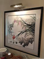 Framed Asian watercolour painting with bamboo style dark wood frame and attached art light above it, showing overall view of artwork on the wall.