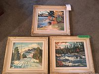 Three framed oil paintings on carpet showing the full set in a group with varying nature scenes.