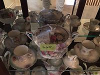 All pieces displayed on glass shelf including covered serving dish, large bowl, orphan lid, and four demitasse sets