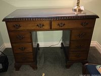 Front view of Honderich wood pedestal desk showing 8 drawers, metal pulls, and glass top.