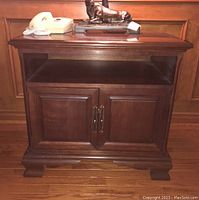 Two matching wood end tables with dark brown finish, each with an open upper shelf, two-door cabinet with metal pull handles, and decorative feet.