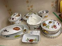 Collection of approximately 11 Royal Worcester Evesham porcelain serving and baking dishes arranged on a counter, featuring fruit and vegetable decorations and gold accents.