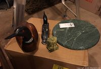 Photo showing all items together: wood carved loon, smaller black stone loon carving signed Jimmy Iqaluq, and circular green stone tray on box surface