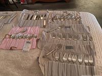 Wide view of multiple cloth rolls holding knives, forks and spoons on a bedspread