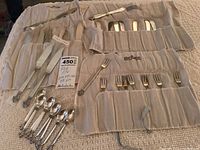 Overview of flatware ensemble rolled in protective cloths showing knives, forks, spoons and anti-tarnish pouches