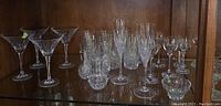 Wide shot showing multiple crystal glasses of various types and sizes, arranged on glass shelf.