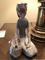 Front and right side view of the porcelain figurine depicting a young girl kneeling with basket and dove, showing details of clothing and posture.