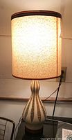 Lamp illuminated showing textured fabric shade and ceramic patterned base