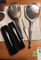 Full view of vanity set items: hand mirror, hairbrush with natural bristles, and cuticle cleaner tool with silver handles on cloth background.