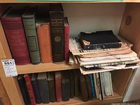 Shelf with vintage hardcover books and stacked papers showing titles and condition.