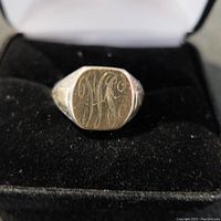 Close-up of silver-toned signet ring with engraved initials inside a jewelry box.