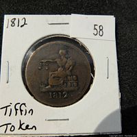 Front side of the 1812 Tiffin Token showing a seated figure with scales and stacks of barrels, with the year 1812 below.
