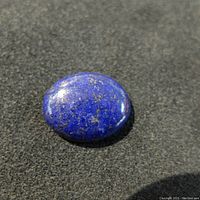 Close-up photo of oval polished lapis lazuli gemstone showing vibrant blue color with gold pine inclusions.